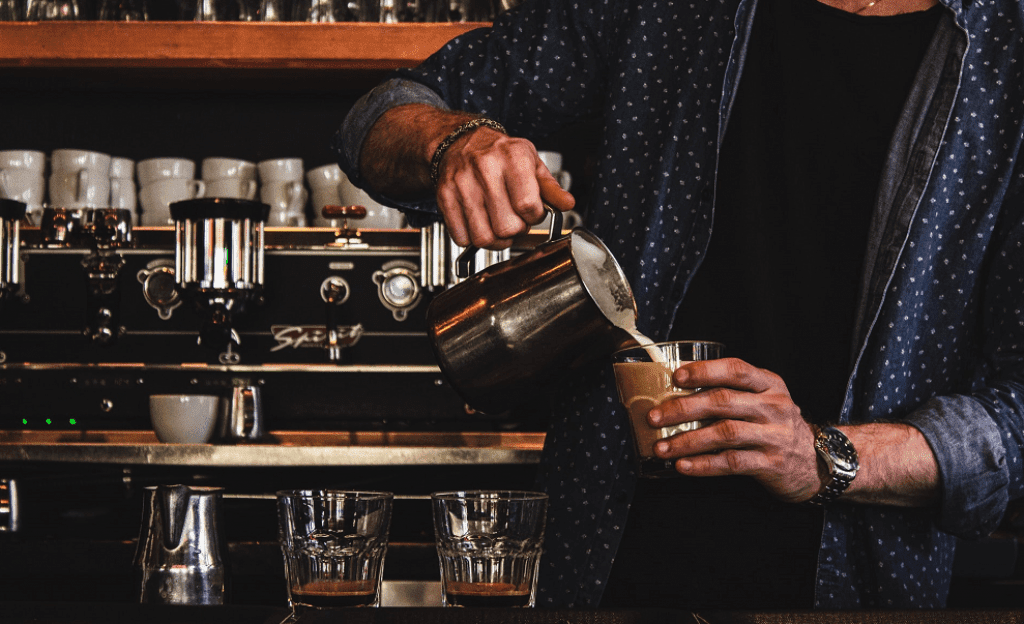 A barista pours milk into an espresso