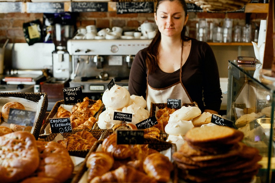 a barista selects baked items to serve coffee shop customers