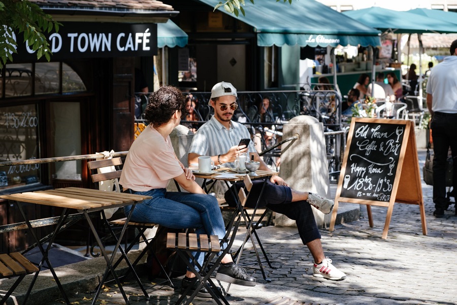 People drink coffee at an outdoor cafe seating area.
