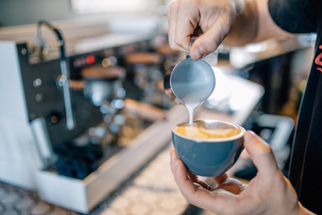 A barista pours a cafe latte from a coffee cart. It looks delicious!