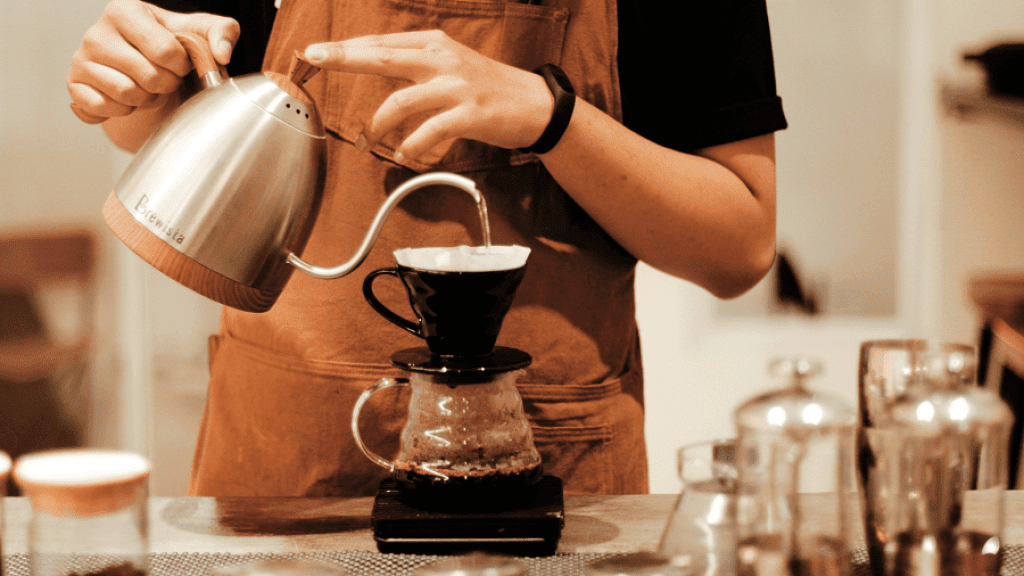 A barista pours a coffee to serve coffee shop customers.