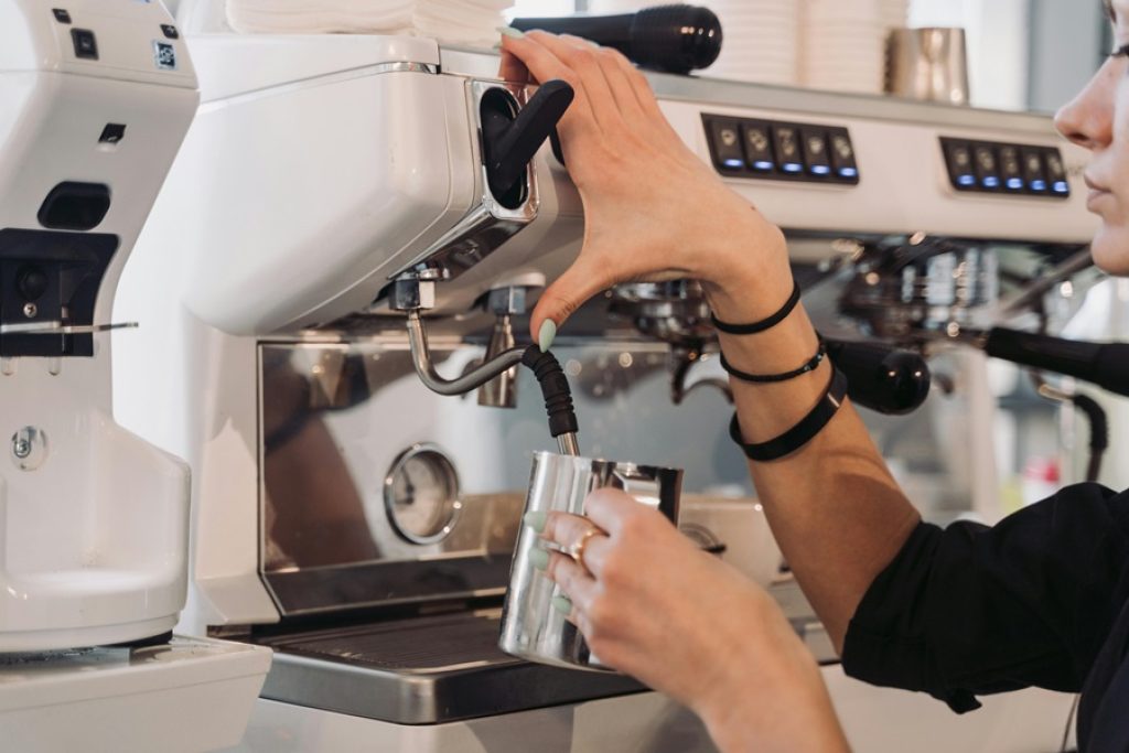 A coffee shop barista serves coffee and steams milk.